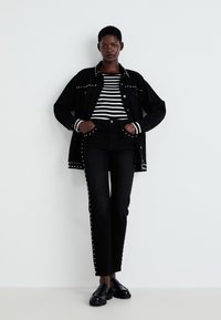 Black denim jacket with studded details, paired with a black and white striped long-sleeve top and black jeans featuring stud accents. Black loafers.
