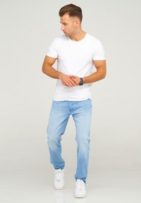 White short-sleeve t-shirt paired with light blue jeans and white sneakers. The fit is casual, with a relaxed design and smooth texture.