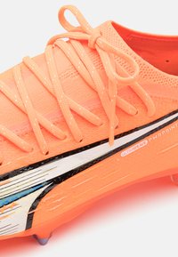 Oranje synthetische voetbalschoen met een gestructureerde bovenkant, dunne veters en zwart-witte ontwerpelementen. Beschikt over een lichte constructie.