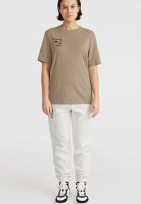 Khaki puuvillane t-särk lühikeste varrukatega ja must "Women of the Wave" graafika. Koos hallide dressipükstega ja musta-valgete jooksujalatsitega.