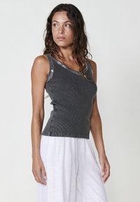 Grijze, geribde tanktop met een V-hals en glinsterende accenten langs de bandjes, gecombineerd met witte, lichte, wijde broekspijpen.