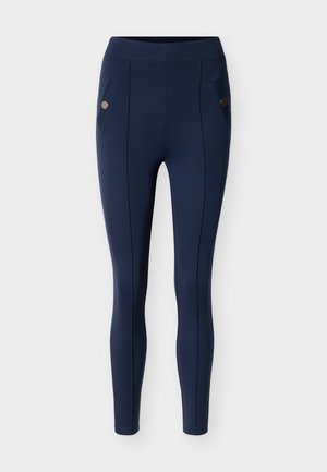 Leggings bleu marine en tissu extensible et lisse. Comprend deux poches avec des accents ronds, des coutures verticales et une taille haute.