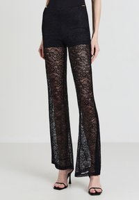 Pantaloni in pizzo nero con vita aderente e design a gamba svasata, con sovrapposizione in pizzo trasparente e dettagli a motivo floreale.