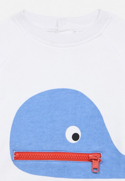 T-shirt blanc pour bébé avec un graphisme de baleine bleue présentant une fermeture éclair rouge comme la bouche de la baleine et un seul œil noir et blanc.