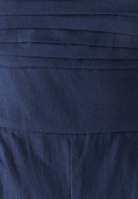 Tkanina mornarsko modre barve z nabrano teksturo in gladkim zaključkom, ki ima vodoravne črte in strukturirano obliko. Brez vidnih kovinskih delov ali poudarkov.