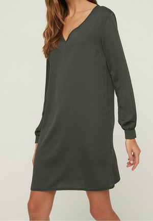 Elegancka ciemnozielona sukienka z dekoltem w serek, długimi rękawami i luźnym krojem. Wykonana z gładkiej tkaniny, z bocznymi szwami i bez widocznych ozdób.