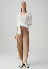 Haut à manches longues blanc avec une ceinture nouée, associé à un pantalon en velours côtelé marron taille haute et des mocassins de couleur claire. Texture lisse.