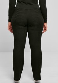 Svart ribbet leggings med en stretchy passform, med høy midje og utsvingt bunn, vist fra bakvinkel.