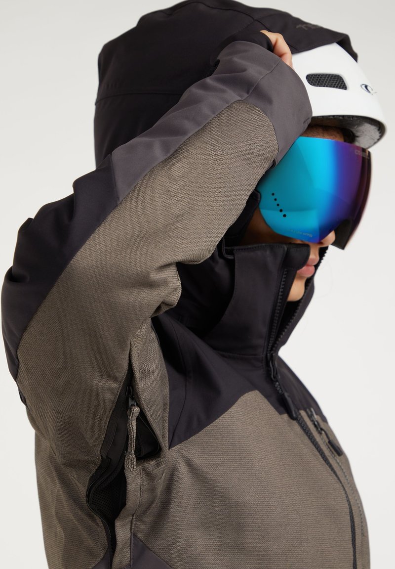 Skijacke aus einer Kombination von schwarzem und strukturiertem grauem Stoff, mit hohem Kragen, Reißverschlusstaschen und verstellbarer Kapuze.