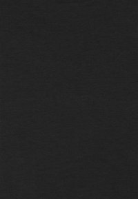 Una giovane donna con capelli ricci, che indossa un blazer grigio e una camicia bianca, sorride mentre è seduta in un ufficio con una sedia grigia e un laptop.