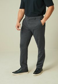 Graue maßgeschneiderte Hose aus glattem Stoff, mit flachem Frontdesign, seitlichen Taschen und schmaler Passform, kombiniert mit schwarzen Sneakern.