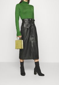 Vihreä, pitkähihoinen pooloneule yhdistettynä mustaan nahkaan valmistettuun midi-hameeseen, jossa on vyötäröllä vyö ja napitettu yksityiskohta. Mustat korolliset nilkkurit.