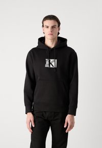 Black hoodie made of cotton blend, featuring a front kangaroo pocket, drawstring hood, and a silver printed CK logo on the chest.