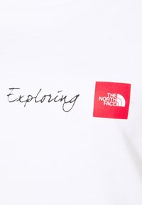White T-shirt featuring "Exploring" in black cursive text and a red square logo with "THE NORTH FACE" in white font. Cotton material.