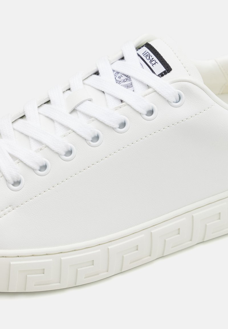 Witte synthetische leren sneaker met een platte profiel, ronde neus, vetersluiting en een geprofileerde, patroon onderkant met een Grieks sleutelmotief.