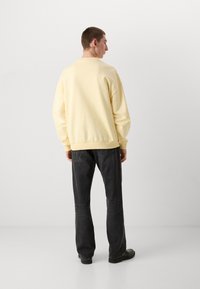 Sweatshirt amarelo claro, ajuste oversized, punhos e bainha canelados, combinado com jeans pretos, textura lisa, design minimalista.