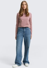 Camisa de manga larga a rayas en rosa claro y malva, combinada con jeans de pierna ancha de talle alto en azul y zapatillas blancas. Diseño simple, ajuste casual.