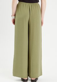 Pantalons larges en vert olive, fabriqués dans un matériau doux, dotés d'une taille élastique et d'une texture lisse. Aucuns motifs ni éléments métalliques visibles.