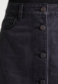 Tmavě modrá džínová sukně s rovný střih, předním zapínáním na knoflíky, pěti kapsami a texturovaným povrchem.