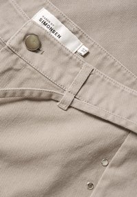 Beige fabric with vertical ribbing and a smooth texture. Features a silver button and brand tag labeled "KAREN BY SIMONSEN."