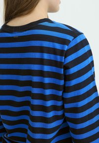 Ribadega mustriga pullover musta ja sinise horisontaalse triibuga, ümar kaelus, pehme kangas ja väike silt ülemises seljas.