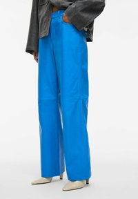 Heledad taevasinised laiad püksid, mis on valmistatud siledast materjalist, kõrge värvli ja küljetaskutega ning stiilse lõikega, kombineeritud teravate beežide kontsadega.