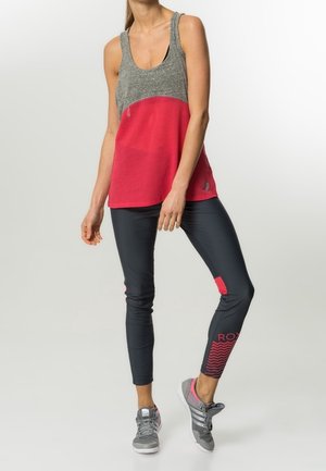 Top con spalline grigio e rosa con texture a rete, abbinato a leggings neri slim-fit con dettagli rosa e logo. Scarpe sportive con tonalità di grigio.