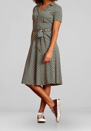 Floral-patterned knee-length dress with short sleeves, collared neckline, cinched waist, and a tie belt, paired with maroon sneakers.