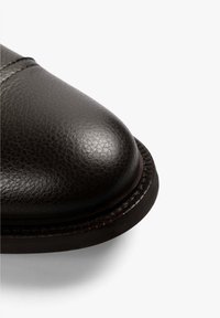 Punta de zapato de cuero negro con forma redondeada y acabado texturizado. Presenta un borde cosido y una superficie lisa y brillante.