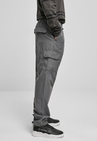 Grijze cargobroek met een elastische tailleband, meerdere zijzakken en een relaxte pasvorm. Gecombineerd met zwarte sneakers met een witte zool.