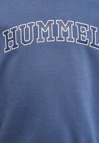 Blauwe katoenen t-shirt met het woord "HUMMEL" in vette, hoofdletter witte letters op de borst, met een gladde textuur.
