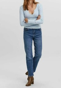 Světle modrý dlouhý rukáv top s kulatým výstřihem, doplněný středně šedými džíny. Hnědé boty na podpatku dokončují outfit.