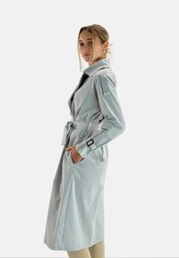 Trench coat grigio chiaro con cintura in vita, spalline, tasche profonde e una texture morbida e liscia.