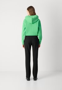 Hanorac verde din bumbac cu glugă, purtat împreună cu pantaloni negri tailored. Ținuta are un design simplu, o textură netedă și detalii minime.