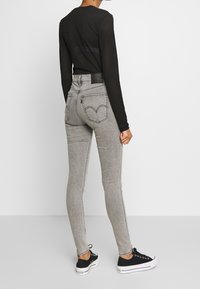 Vaqueros grises de tiro alto con ajuste slim, que cuentan con bolsillos desgastados y un parche trasero de cuero negro. Combinados con zapatillas negras.