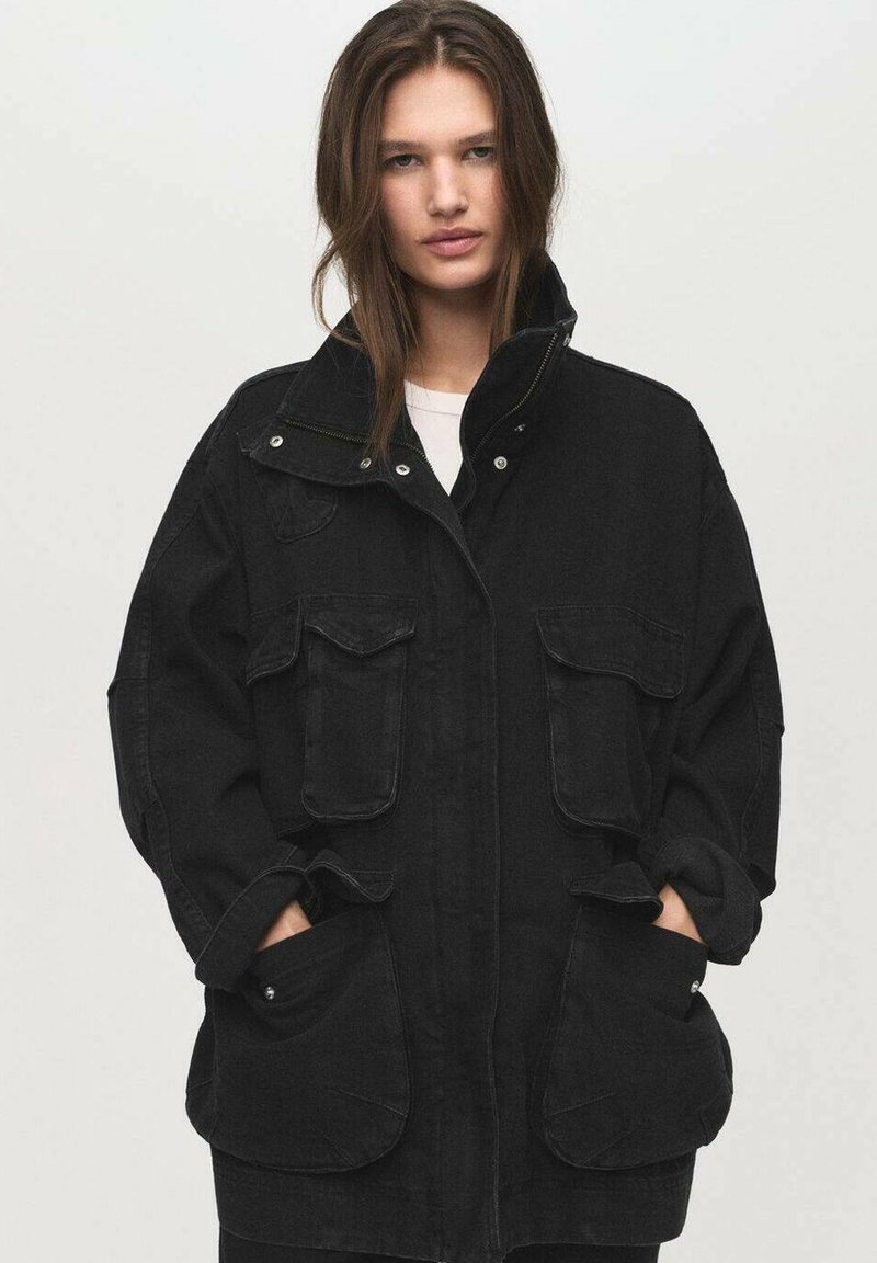 Zwarte oversized denim jacket met twee grote voorkruiszakken, een hoge kraag en knoopdetails. De stof lijkt stevig met een lichte textuur.