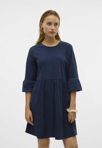 Mörkblå klänning i knälängd med rund halsringning och 3/4-långa ärmar som har volangärmar och ett rynkat midjeband. Slät textur.