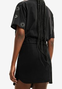 Svart kortärmad t-shirt med spiralbroderi på ärmarna, tillsammans med en svart minikjol med ett texturerat bälte.