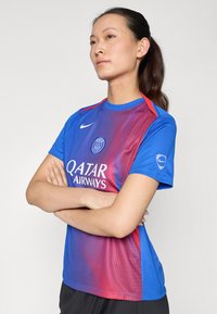 Mėlyna ir magenta sportinė marškinėlė su apvaliu kaklu, turinti „Nike“ logotipą, „Qatar Airways“ tekstą ir dryžuotą dizainą priekyje.
