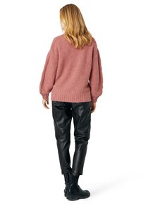 Maglione rosa soffice con spalle scese e orlo a coste, abbinato a pantaloni in finta pelle neri e stivali neri chunky.