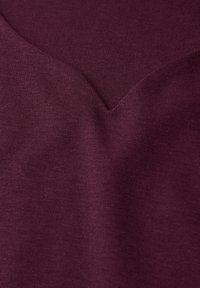 Burgundská látka s hladkým povrchem a véčkovým výstřihem. Materiál vypadá jako pletený a je měkký s rovnoměrným rozložením barvy.