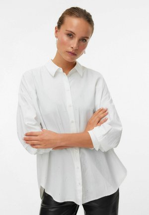 Chemise blanche à boutons avec col, manches longues et coupe légèrement ample. Présente des accents de perles discrets et une texture lisse.