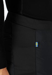 Zwarte gewatteerde broek met een gladde textuur, voorzien van een klein accent van de Zweedse vlag in blauw en geel aan de zijkant.