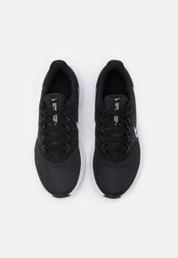 Zapatillas deportivas negras con parte superior de malla, cierre de cordones y acentos blancos en el swoosh y la suela. Cuenta con una plantilla acolchada para mayor comodidad.