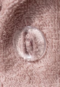 Pink, textured fabric with a fuzzy surface and a clear, round plastic button featuring two holes sewn onto it.