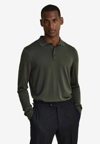 Olijfgroene polo met lange mouwen en kraag, voorzien van een twee-knopen sluiting en een zachte textuur, gecombineerd met zwarte broek.