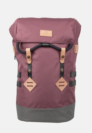 Sac à dos avec rabat roulé violet et gris avec fermeture à corde noire, accents en cuir beige et étiquette frontale indiquant "Doughnut".