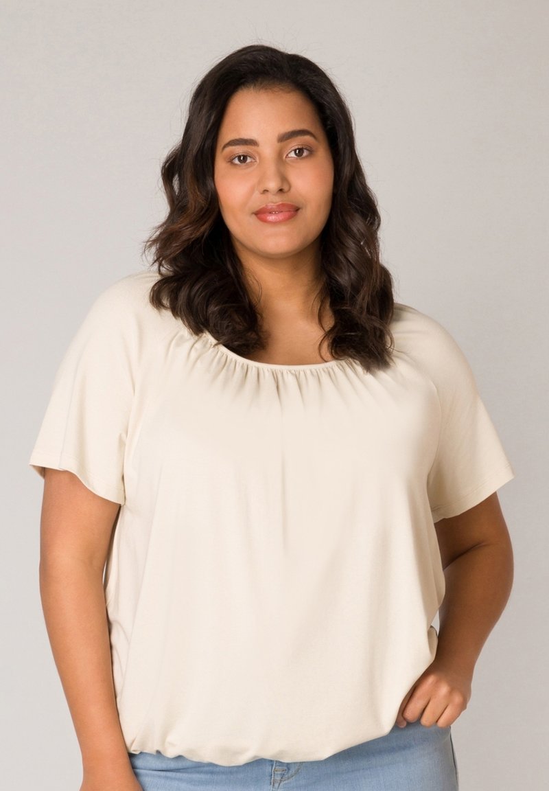 Beige short-sleeve top with a scoop neck and gathered detailing at the neckline, paired with light-wash denim pants. Smooth texture.