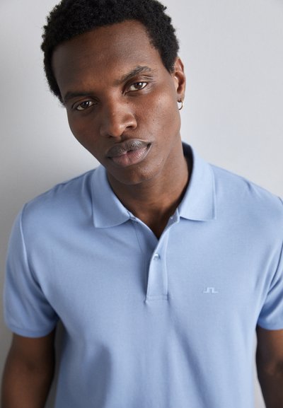 Light blue cotton polo shirt with a collar, three buttons, and a small logo on the chest. Smooth texture and fitted design.