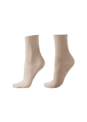 Paire de chaussettes montantes beige côtelées montrées de profil sur un fond blanc.